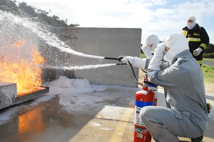 Defence personnel in protective suits using foam on a fire during firefighting training, a source of PFAS contamination